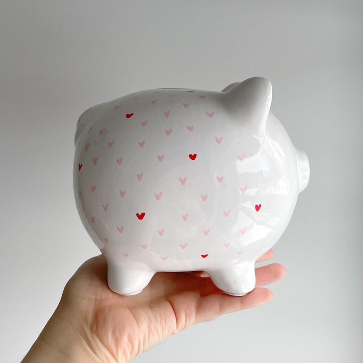 a hand holding a white ceramic pig with hearts on it