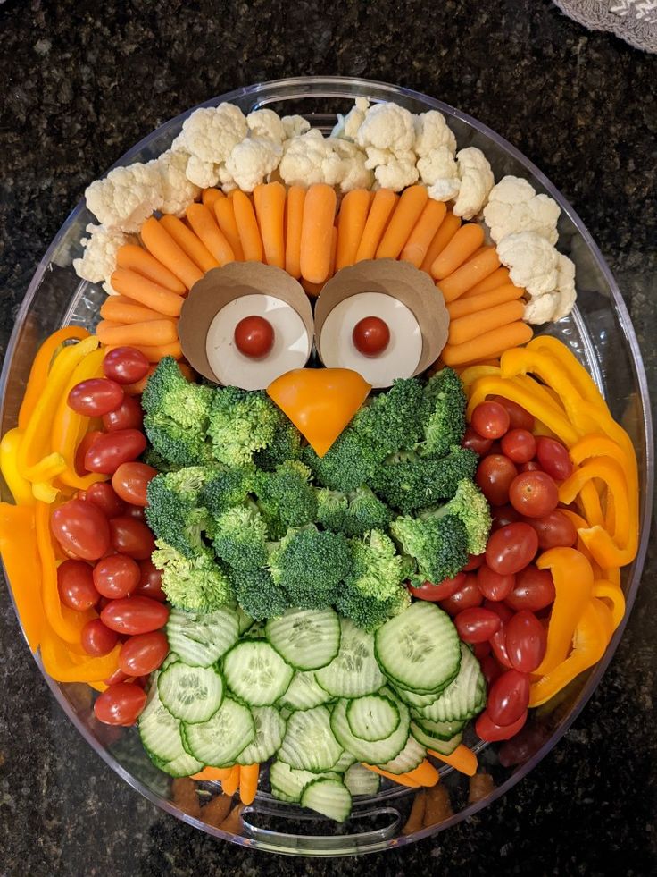 an owl made out of fruits and vegetables on a platter with eyes, carrots, broccoli, cauliflower, cucumbers