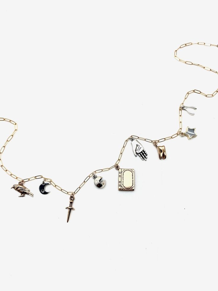 The perfect charm necklace for the mystic, fantasy, book-loving, mixed-metal wearer! We love this dainty yet meaning-packed necklace! Features 9 unique charms, delicately strung on a gold-filled paper-clip chain bronze tiny raven sterling crescent moon bronze dagger sterling fortune cookie bronze book sterling open palm, or blessing hand solid bronze tiny tooth mother-of-pearl star, electroplated in 18K gold sterling wishbone Details: 18" paperclip chain, 1/20 18K gold-filled. Charms alternate b Mystical Adjustable Moon Charm Necklace, Dainty Brass Charm Necklace With Lobster Clasp, Celestial Crescent Charm Necklaces, Gold-tone Metal Charm Necklaces, Dainty Brass Moon Charm Necklace, Elegant Brass Charm Necklace With Moon Charm, Mystical Moon Charm Brass Necklace, Open Palm, Knife Necklace