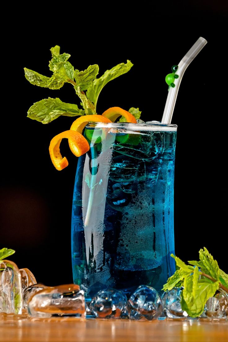 a blue drink with orange peels and mint on the rim, in a glass