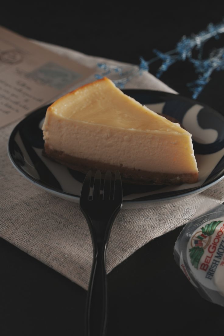 a piece of cheesecake on a black and white plate with a fork next to it