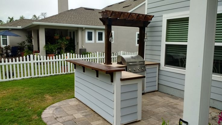 an outdoor bbq and grill area in front of a house with a white picket fence