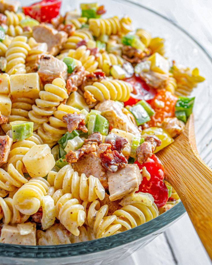 a pasta salad with chicken and vegetables in a glass bowl