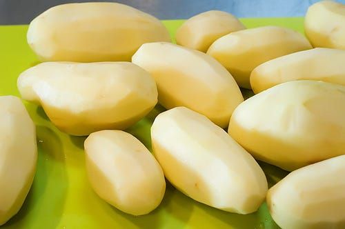 a green cutting board topped with peeled potatoes