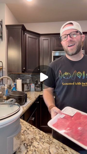 a man holding a tray with raw meat on it in a kitchen next to a sink