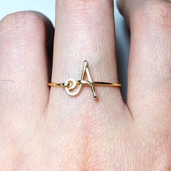 a woman's hand with a gold ring on top of her finger and the letter a in the middle