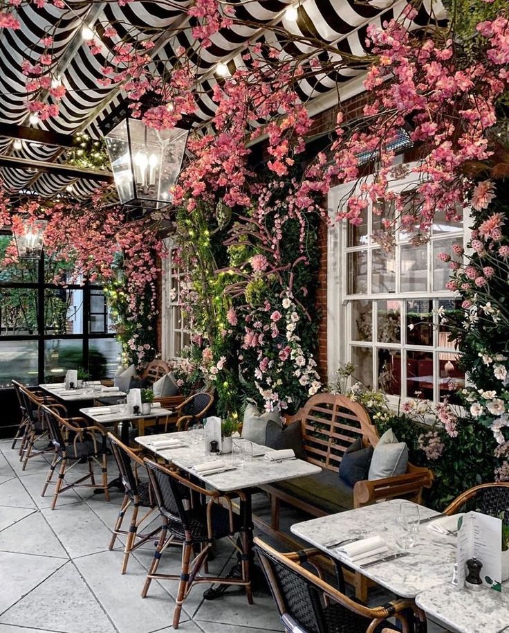 an outdoor dining area with tables and chairs covered in pink flowers on the ceiling, along with large windows