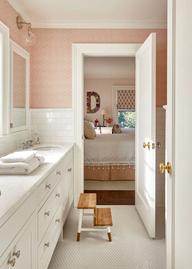 an open door leading to a bathroom with two sinks and a bed in the background