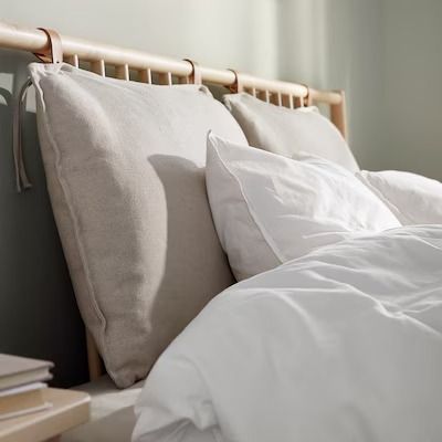 a bed with white linens and pillows on it's headboard, next to a window