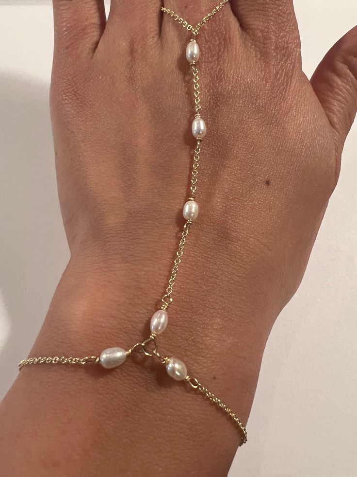 This genuine Pearl hand chain is Stunning and made by hand using genuine Swarovski rhinestones and crystals, 14k gold fill chain and clasp. Made for the Ti Adora by Alvina Valenta 2016 NY Bridal Market and LookBook photoshoot. Typical made for a 7" long hand (wrist to top of center finger):6.5" in wrist circumference with .5" additional adjustable clasp.3" from wrist up to the ring2.5" in ring loop circumference (non adjustable)Custom length is welcome! Just write in the measurements in the note Bracelet Connected To Ring, Ring To Bracelet Jewellery, Diy Hand Chain, Gold Plated Silver Jewelry With Pearl Charm, Pearl White Metal Jewelry With Adjustable Chain, Silver Gold Plated Jewelry With Pearl Charm, Round Pearl Chain Jewelry, Dainty Metal Jewelry With Pearl Charm, Wedding Pearl Bracelet With Metal Charm