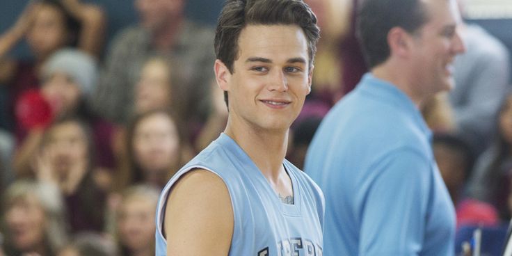 a young man standing in front of a crowd wearing a blue shirt and smiling at the camera