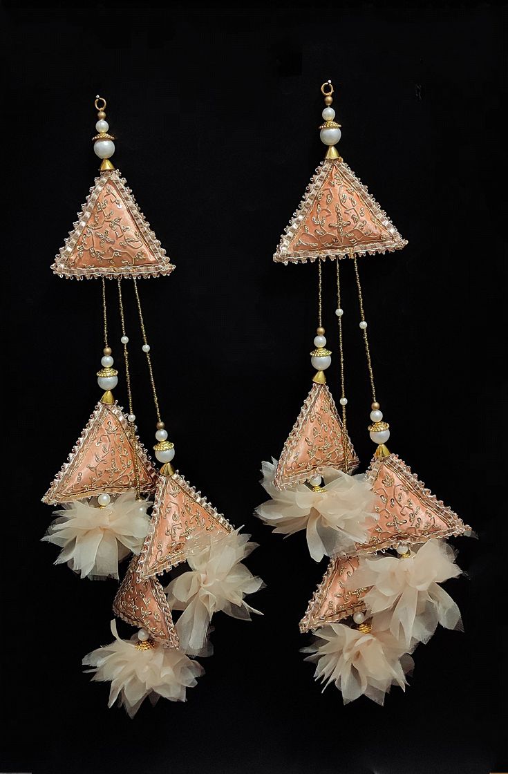 two pairs of earrings with pearls and feathers hanging from it's sides on a black background