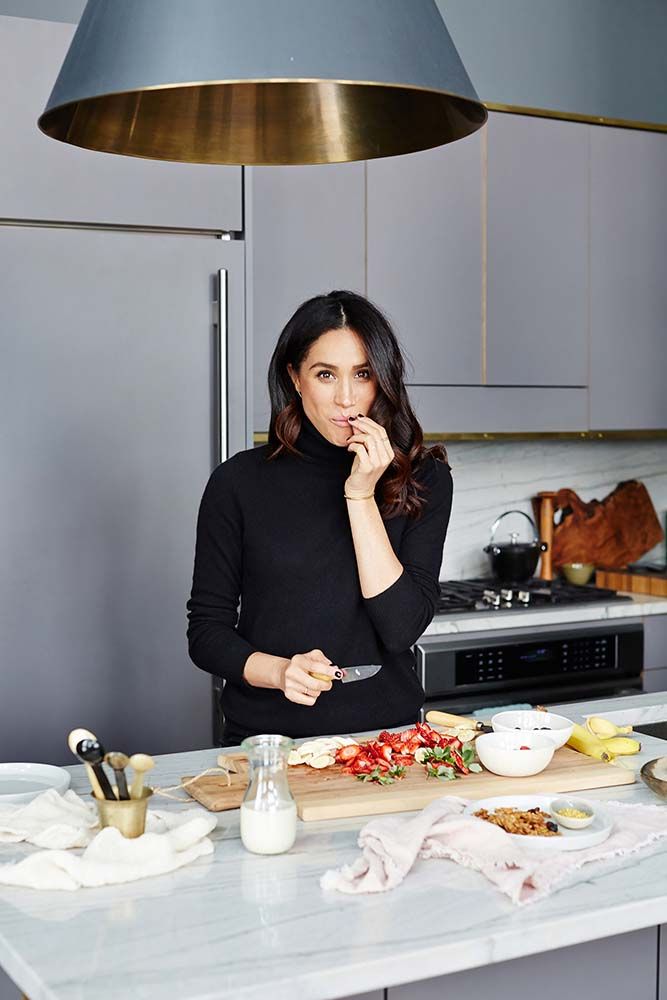 a woman standing at a kitchen counter with food in front of her and a lamp above her