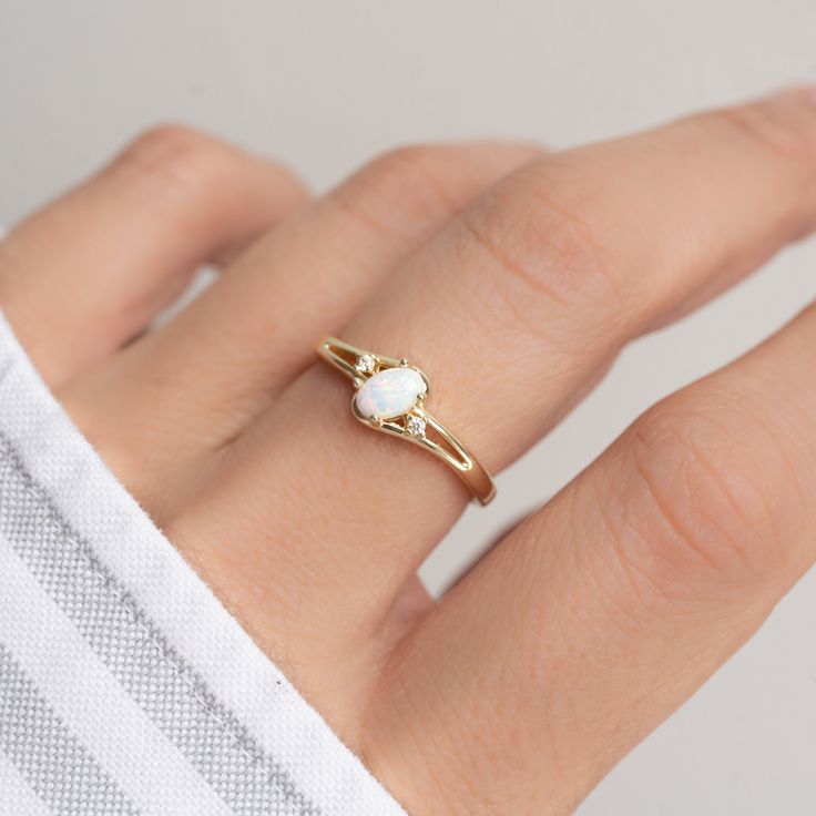 a woman's hand wearing a gold ring with a white stone