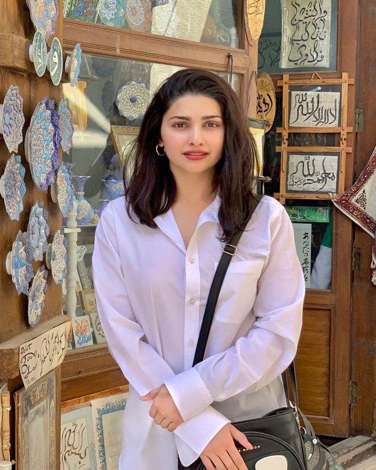 a woman standing in front of a store holding a handbag and posing for the camera