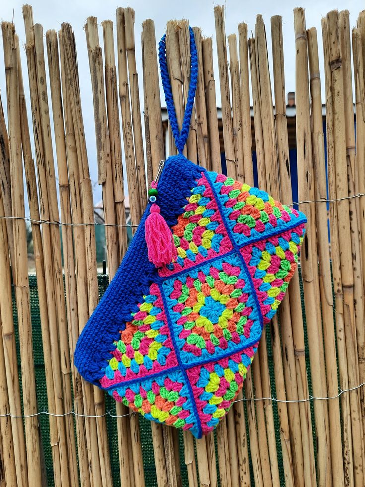 a crocheted purse hanging on a fence made of bamboo sticks and wood poles