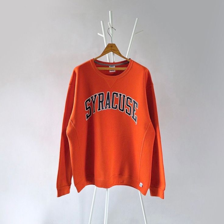 an orange sweatshirt hanging on a white hanger with the word syracsie printed on it