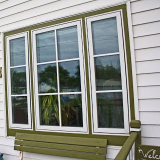 a wooden bench sitting in front of a white house next to a green door and window