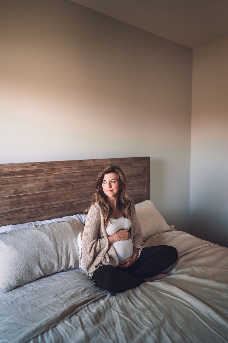 a woman sitting on top of a bed with her stomach in the air while holding a baby bump