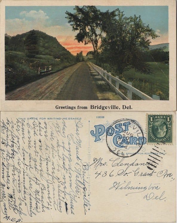 an old postcard with some writing on the front and back side, along with a photo of a country road in the background