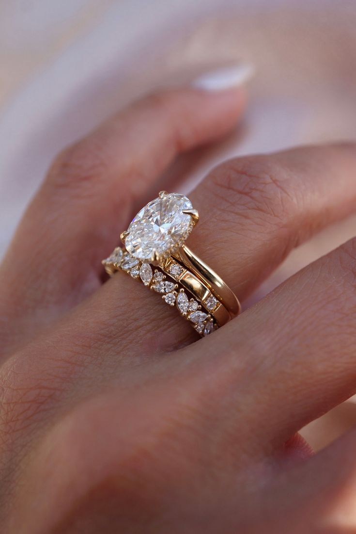 a woman's hand with a gold ring and two diamond engagement rings on it