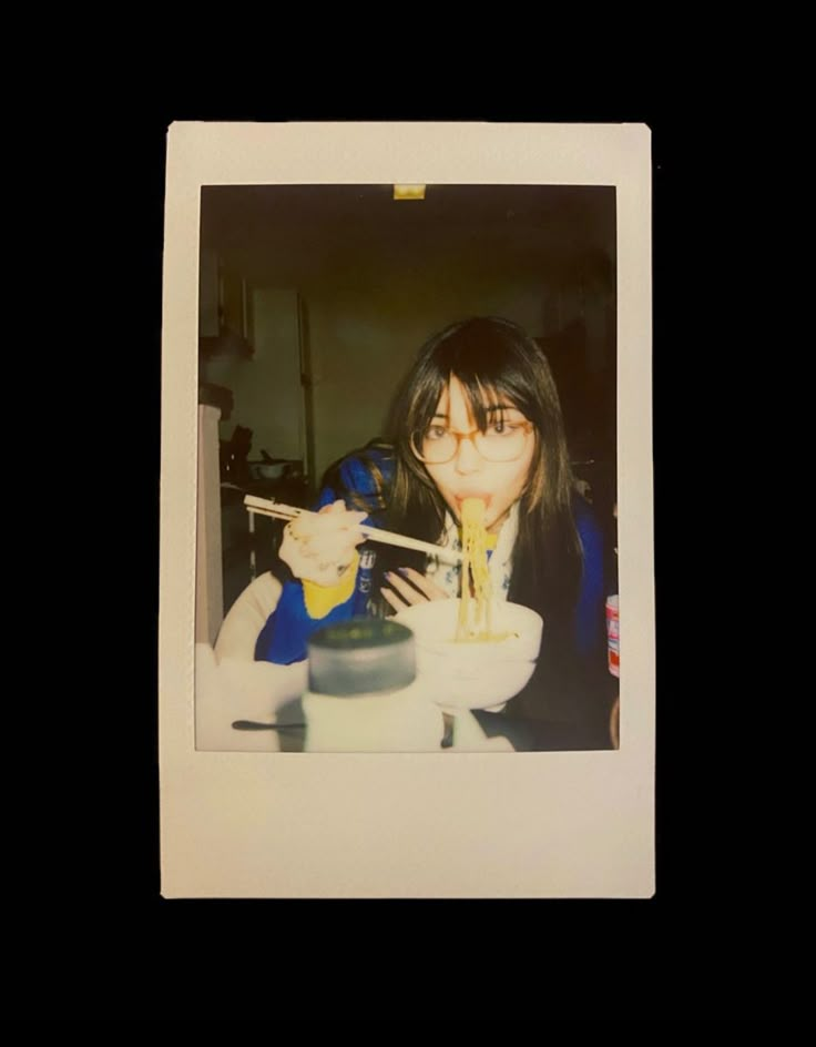 a woman eating noodles with chopsticks in her hand while sitting at a table