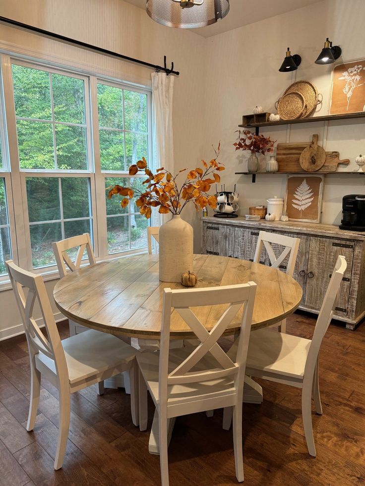 a dining room table with chairs and a vase on top of it in front of a window