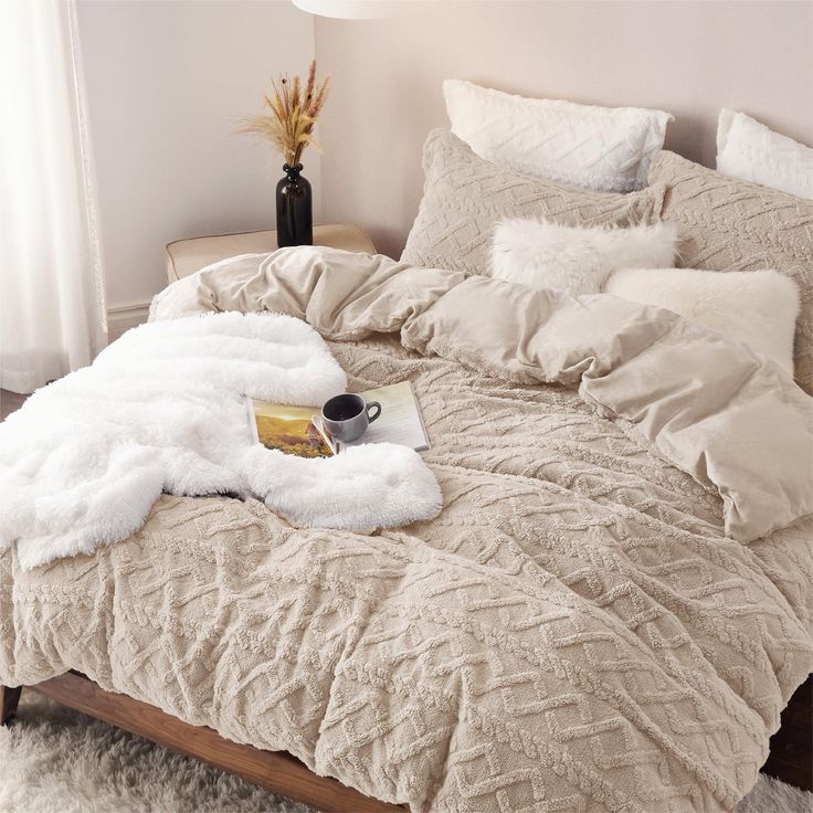 a bed with white comforter and pillows on it, next to a vase filled with flowers