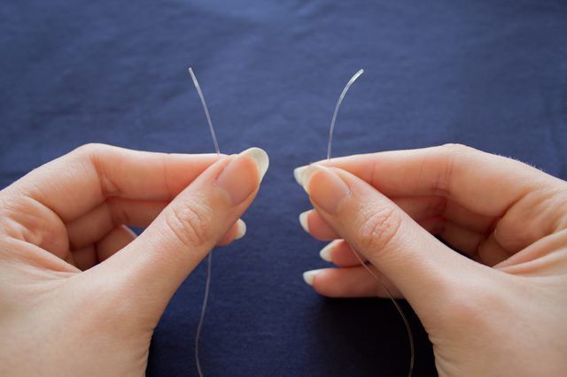 two hands are holding thread on a blue surface