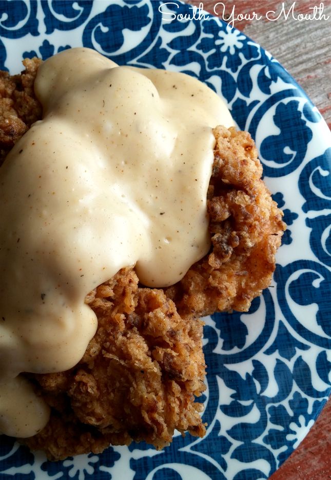 a blue and white plate topped with fried chicken covered in gravy on top of a wooden table