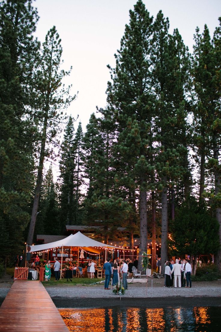 people are gathered at the end of a dock near some trees and tents with lights on them