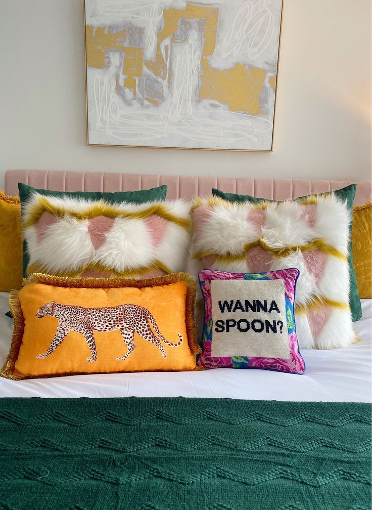 two pillows on top of a bed with an animal pillow next to it and a painting above