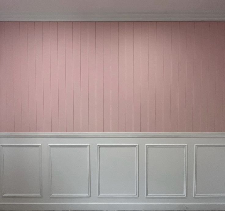 an empty room with pink walls and white paneling on the wall, in front of a bench