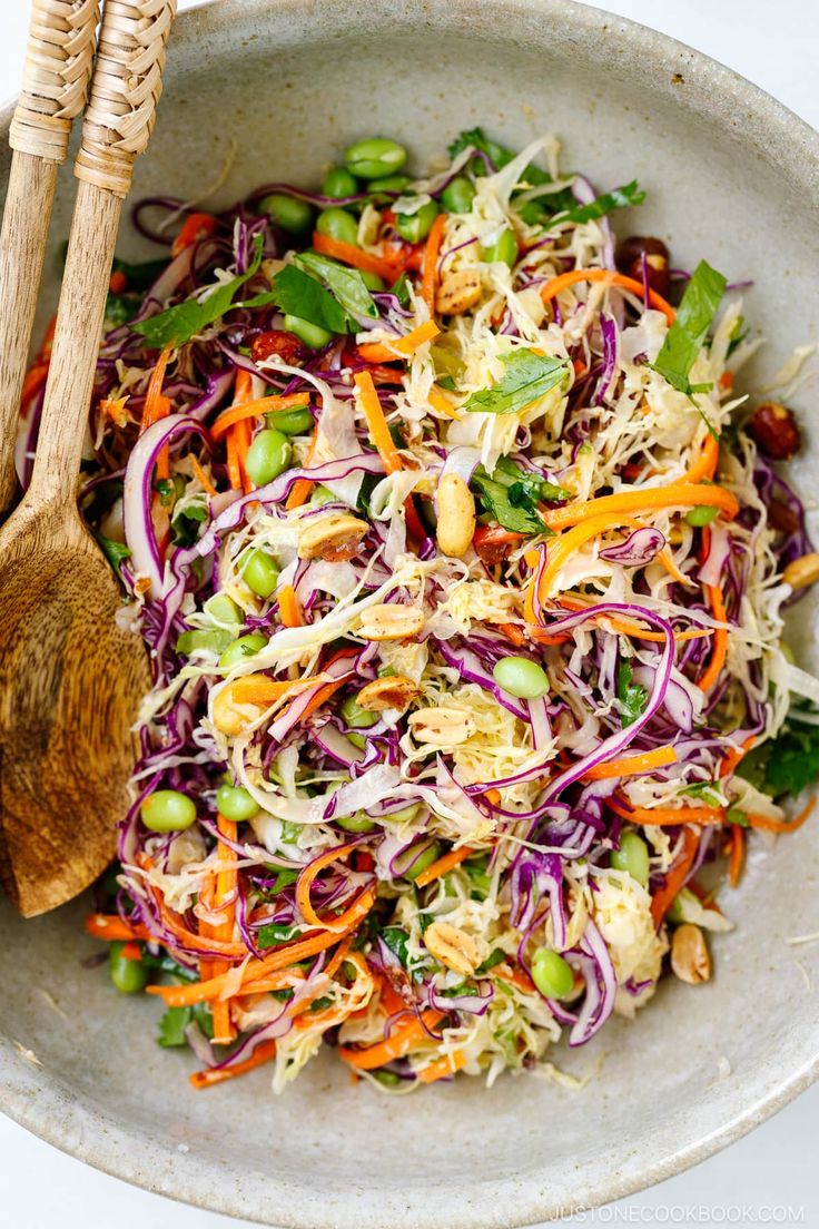 a bowl filled with coleslaw and carrots next to two wooden spoons