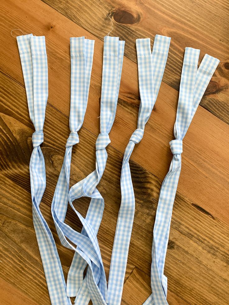 four pieces of blue and white gingham ribbon on a wooden table with scissors