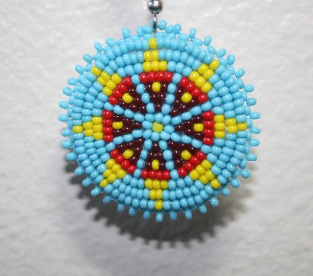 a beaded ornament hanging from a metal hook on a white wall with blue, yellow and red beads