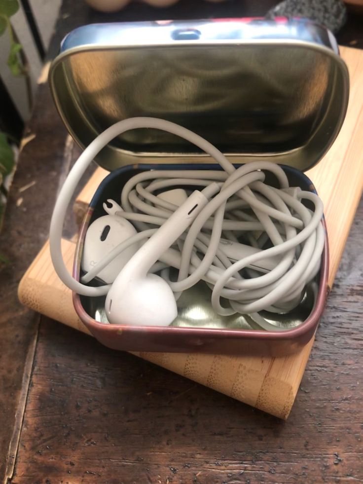 an open tin can filled with cords and plugs on top of a wooden table