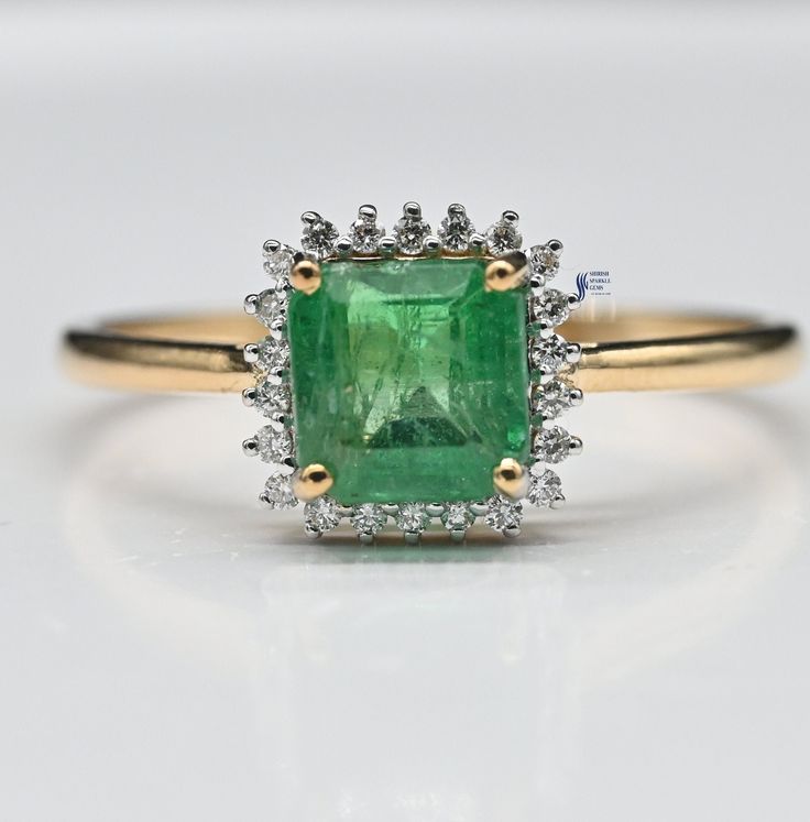 an emerald and diamond ring on a white surface