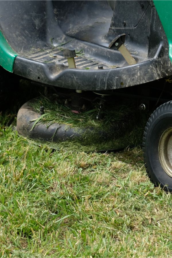 a green lawn mower sitting on top of a lush green grass covered field next to a tire