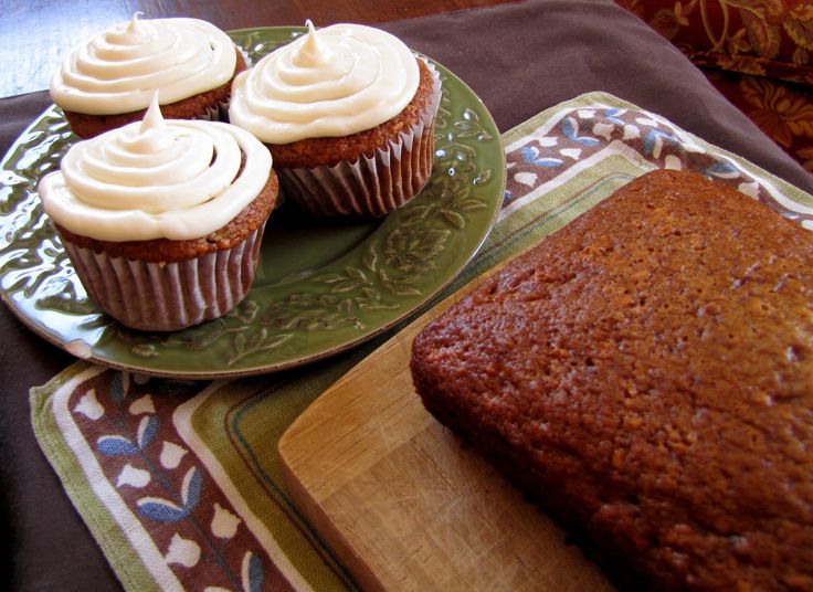 three cupcakes and a loaf of cake on a plate next to a cutting board