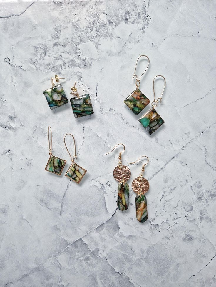 four pairs of earrings sitting on top of a marble surface