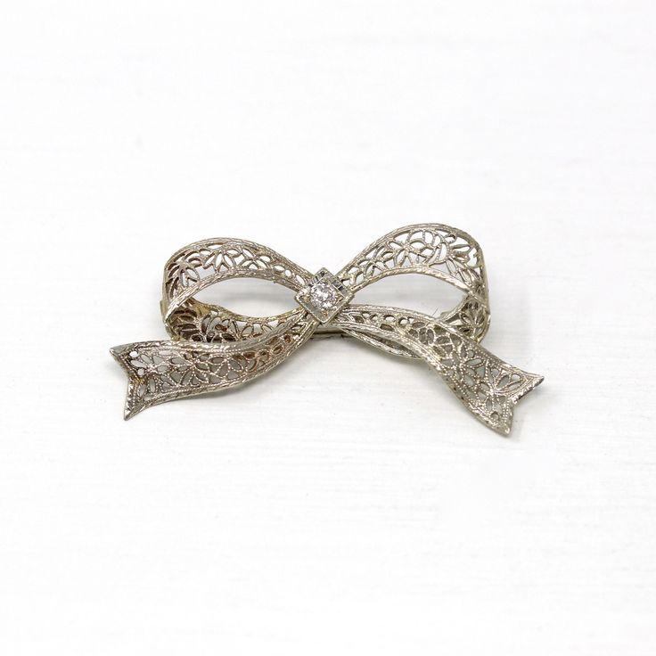 Gorgeous vintage circa 1930s era 14k white gold diamond bow brooch! This beautiful piece showcases a sparkly old European cut diamond center weighing an estimated .07 carats. The setting features ornate flower filigree with milgrain details. The brooch secures with a rotating c-clasp. An outstanding Art Deco Era piece of fine jewelry! *Sale - price reduced from $340 USD to $330 USD.  ERA - Circa 1930s - Art Deco  METAL / MATERIAL - 14k white gold, 1 old European cut diamond (estimated .07 cts, SI2, near colorless)  MARKINGS / HISTORY - Brooch clasp marked "14k"  CONDITION - Good antique condition. White gold metal has been professionally polished & cleaned. Very light age appropriate patina & wear remains. Amazing vintage bow brooch!  SIZE / MEASUREMENTS - Brooch: 1 1/2 x 3/4 inches, Weigh Vintage Platinum Brooches With Diamond Accents, Vintage White Gold Platinum Brooches, Vintage Platinum White Gold Brooches, Vintage Platinum Brooch In White Gold, Art Deco Platinum Brooches For Anniversary, Antique White Gold Brooches For Wedding, Vintage White Gold Brooches With Diamond Accents, Vintage Platinum Brooches For Formal Wear, Vintage Platinum Brooches For Formal Occasions