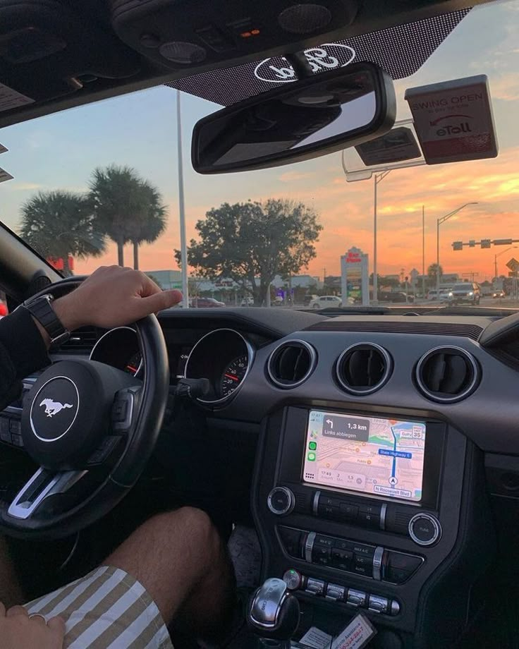 a man is driving his car with the sun setting in the background