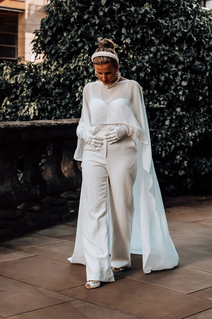 a woman in white is walking down the street wearing a long sleeved top and wide pants