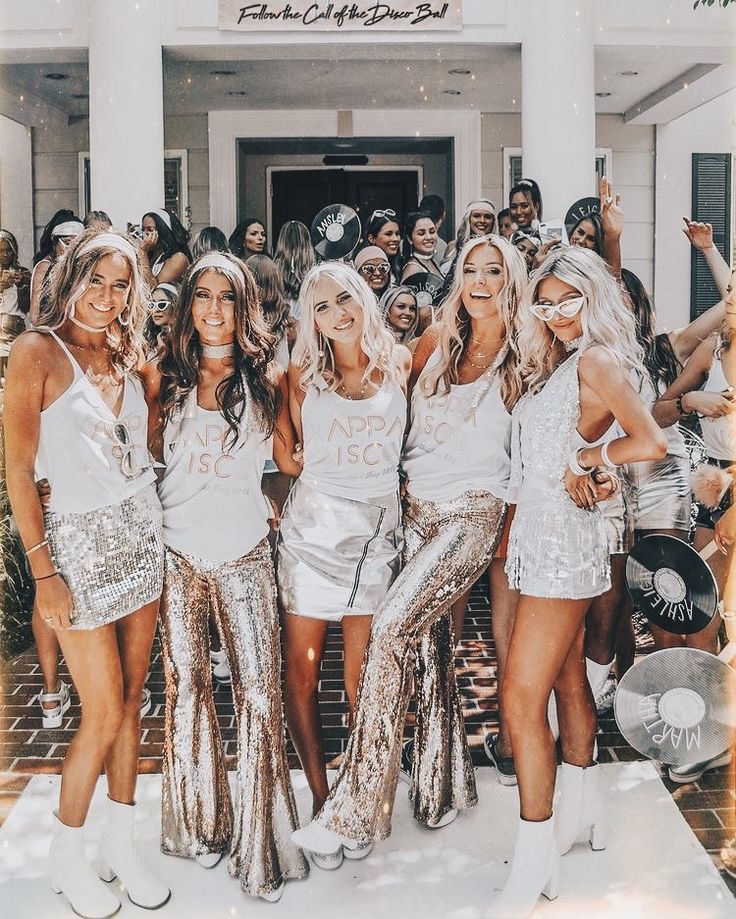 a group of women standing next to each other in front of a white building with gold sequins