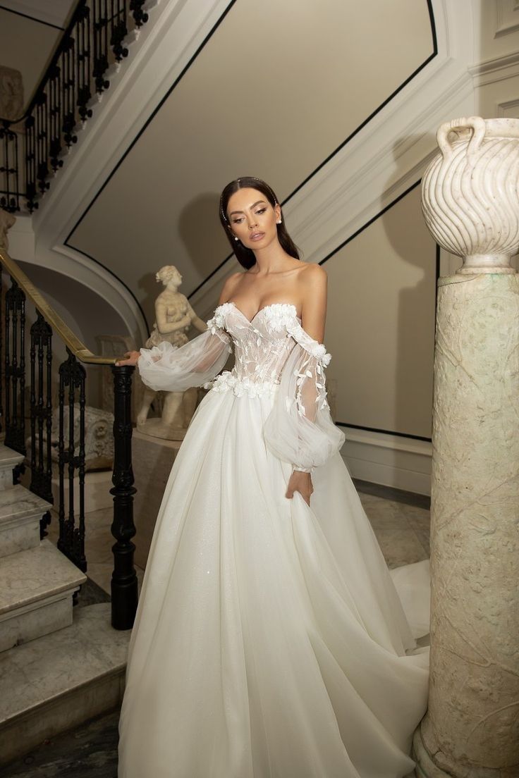 a woman in a white wedding dress standing next to a stair case and looking at the camera