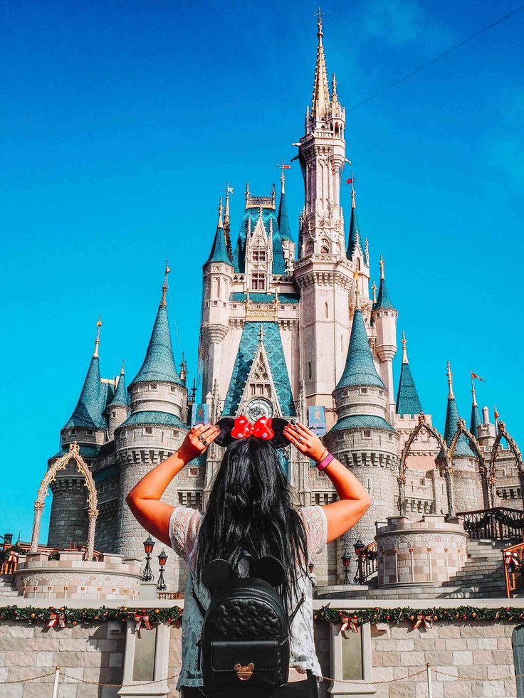 a woman standing in front of a castle with her hands on her head looking at the sky