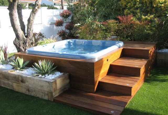 a hot tub sitting on top of a wooden deck next to a lush green yard