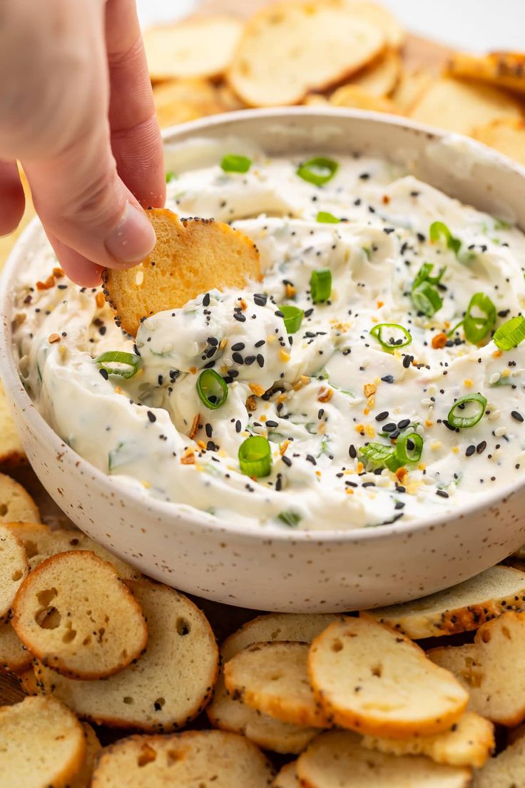 a hand dipping a cracker into a bowl of white dip surrounded by crackers