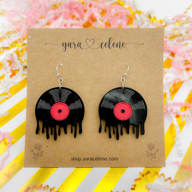 black and red vinyl record earrings with drips on them sitting on top of a card